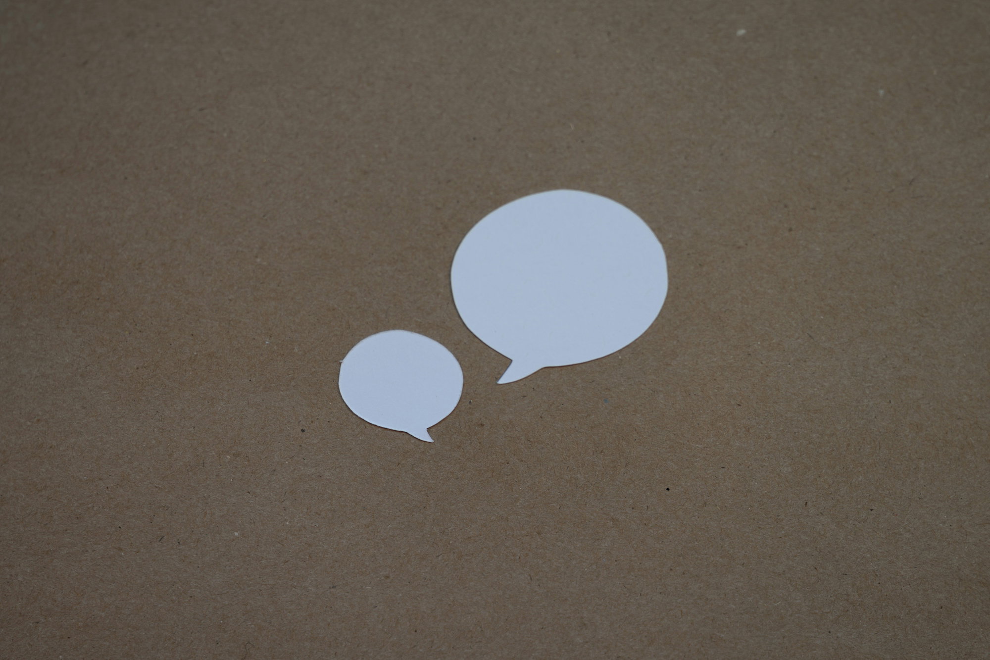 two white speech bubbles sitting on top of a brown surface